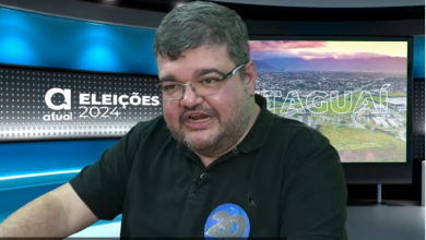 Rubão, de óculos e blusa preta, tendo ao fundo um cenário com a logomarca do jornal atual com a inscrição Eleições 2024 à esquerda e Itaguaí à direita