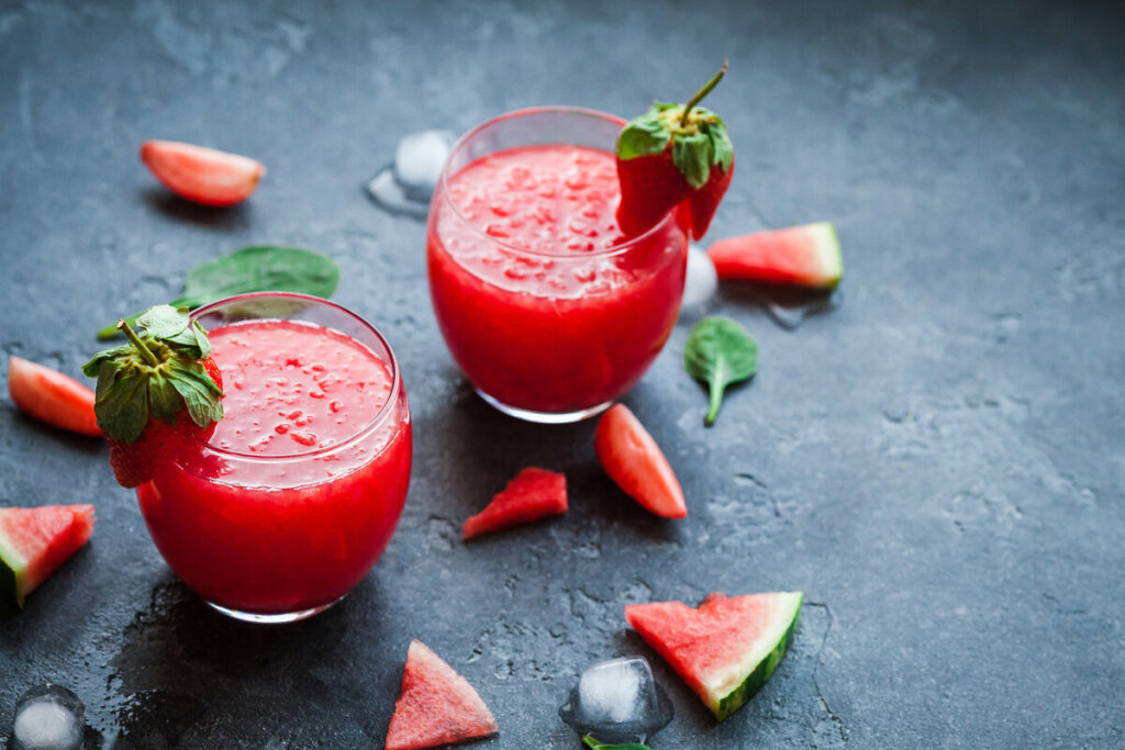 Copo de vidro com suco de melancia e morango, decorado com pedaços de morango em cima de uma mesa 