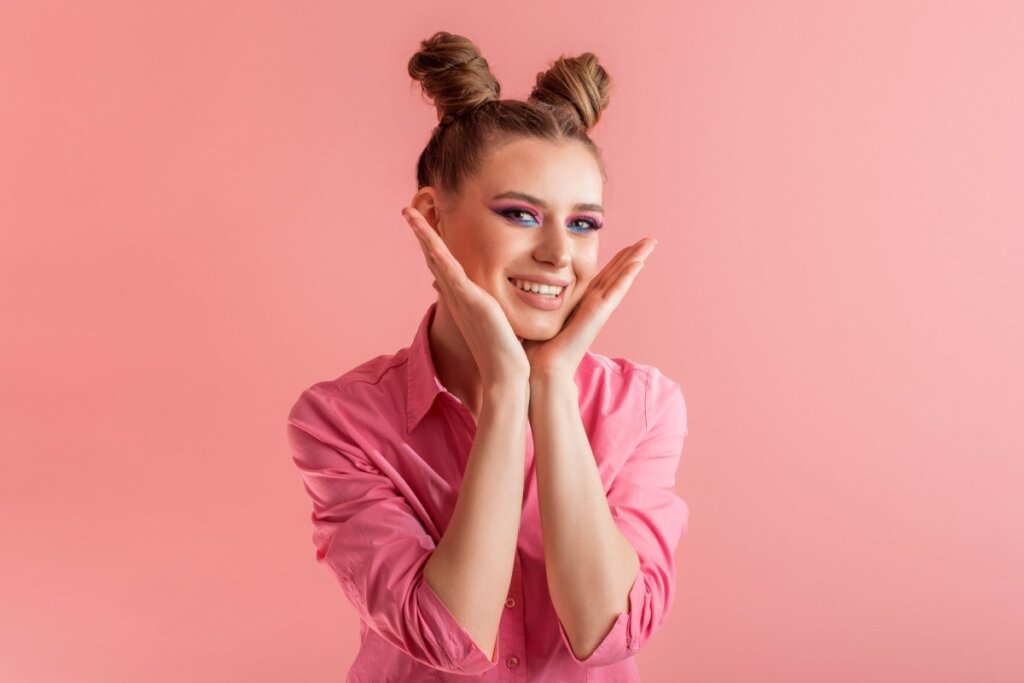 Mulher usando maquiagem colorido, sorrindo e usando um coque "space buns" no cabelo 