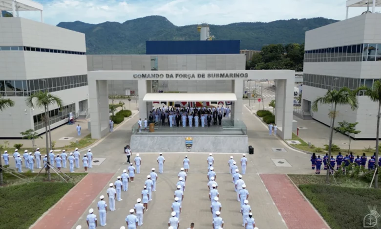 Marinha do Brasil expande Complexo Naval de Itaguaí - foto aérea mostra cerimonial. No primeiro plano, militares estão em posição de sentido enfileirado. No cenário, ao centro tem um portal com a inscrição "comando da força de submarinos" entre dois prédios administrativos, onde estão os militares de alta patente