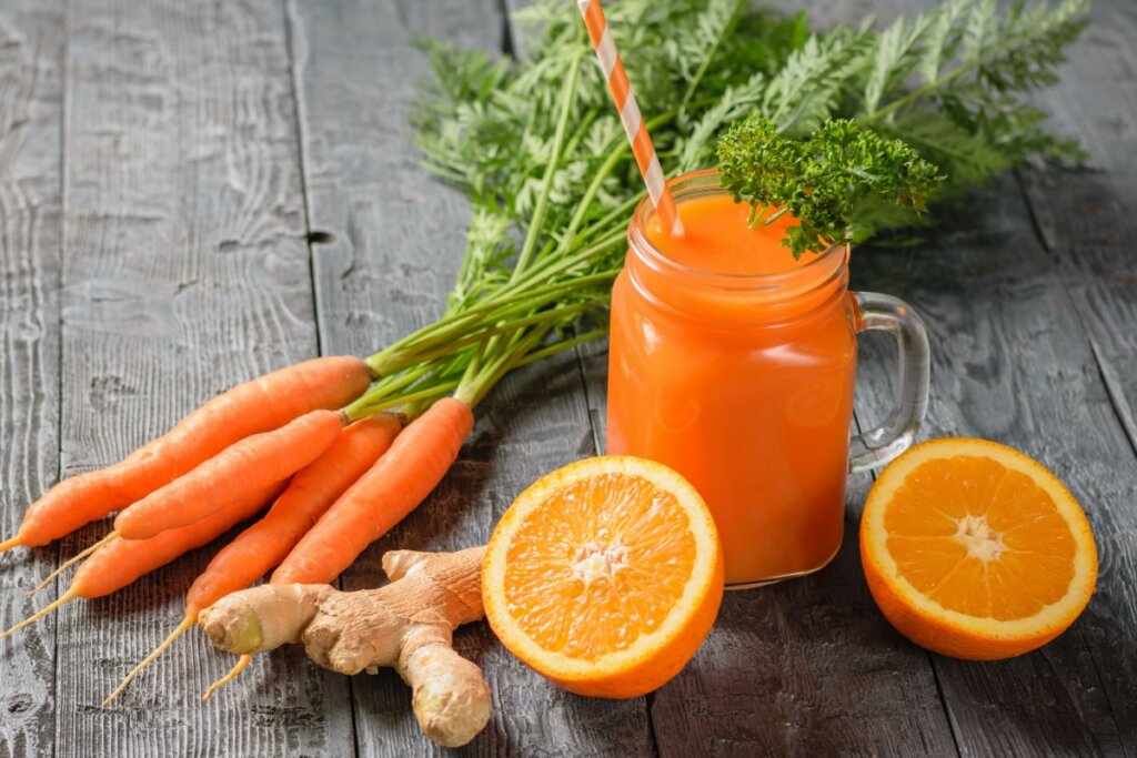 copo de vidro com suco laranja e cenoura, laranja e gengibre em volta