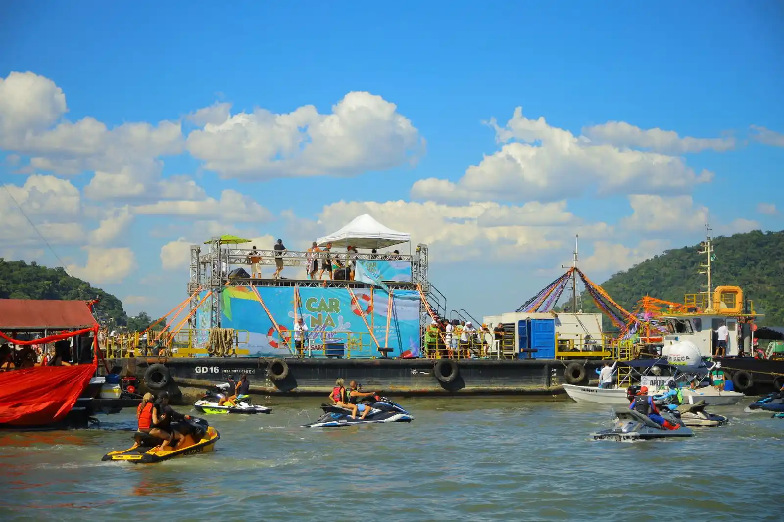 Carnamar 2025 Mangaratiba / foto tem no centro a embarcação da organização com uma faixa inscrita Carnamar 2025 - Mangaratiba, com outras pequenas embarcações no entorno