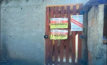Avisos de "Obra Embargada" e "Notificado e Multado" são afixados em portão de construção irregular