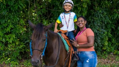 Criança em cima do cavalo com a professora em pé ao lado durante a equoterapia