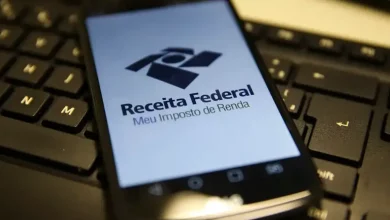 Celular com tela ligada no aplicativo da Receita Federal está deitado em cima de um teclado de computador.