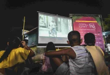 Crianças sentadas na rua assistindo um filme em uma projeção na parede
