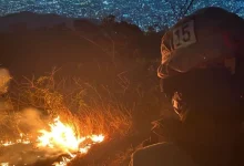 Bombeiro observa foco de incêndio em área de vegetação seca durante a noite