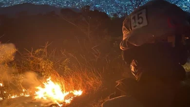 Bombeiro observa foco de incêndio em área de vegetação seca durante a noite