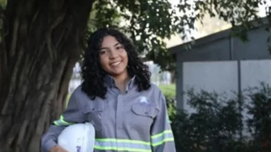 Estagiária uniformizada sorrindo com capacete embaixo do braço