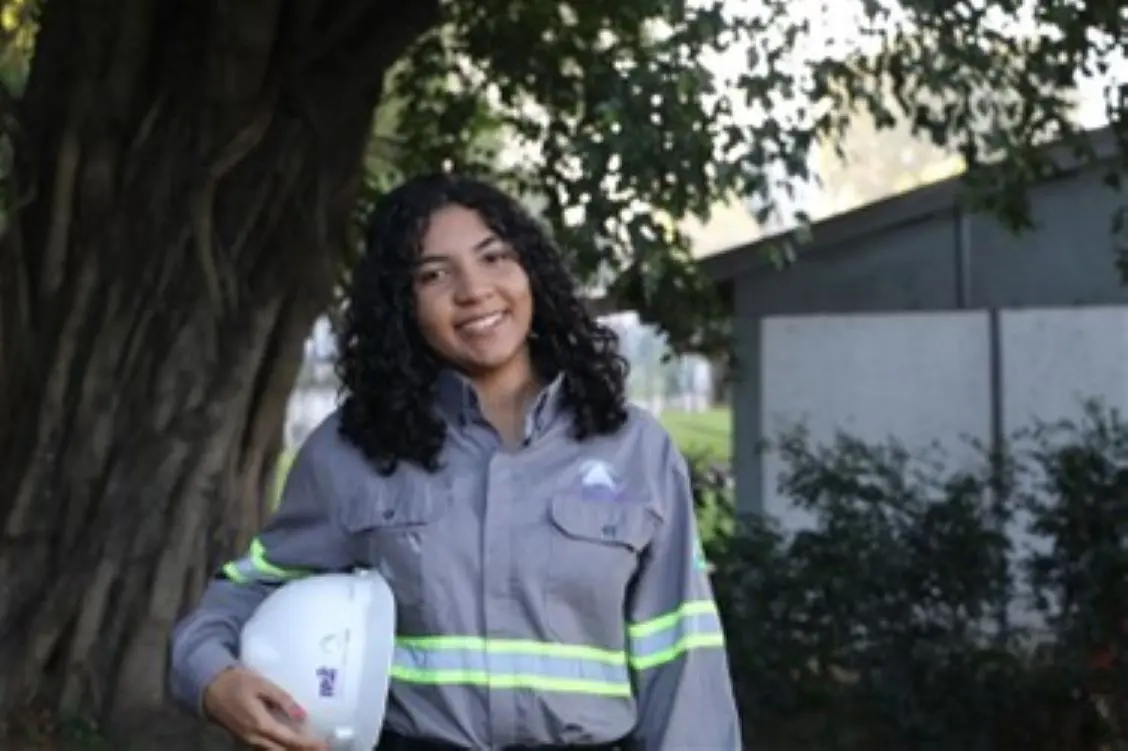 Estagiária uniformizada sorrindo com capacete embaixo do braço