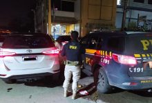 Agente entre o carro recuperado e a viatura da PRF em frente a delegacia de Seropédica