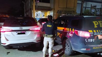 Agente entre o carro recuperado e a viatura da PRF em frente a delegacia de Seropédica