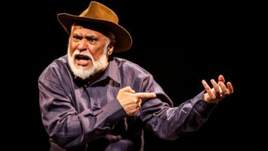 Cena do espetáculo “O Julgamento de Zé Bebelo”, com ator caracterizado como sertanejo gesticulando em palco escuro.