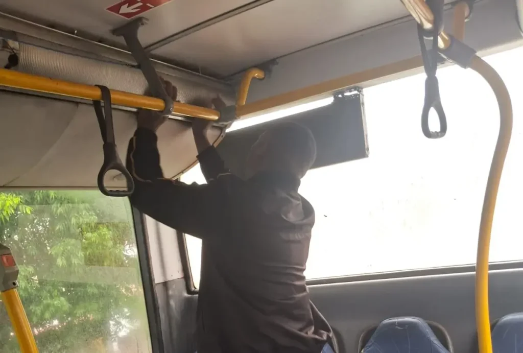 Homem tentando prender estrutura no teto do ônibus