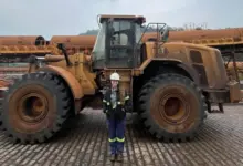 Colaboradora posando para foto em frente a uma máquina móvel pesada