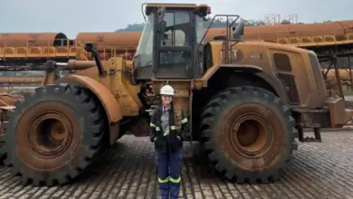 Colaboradora posando para foto em frente a uma máquina móvel pesada