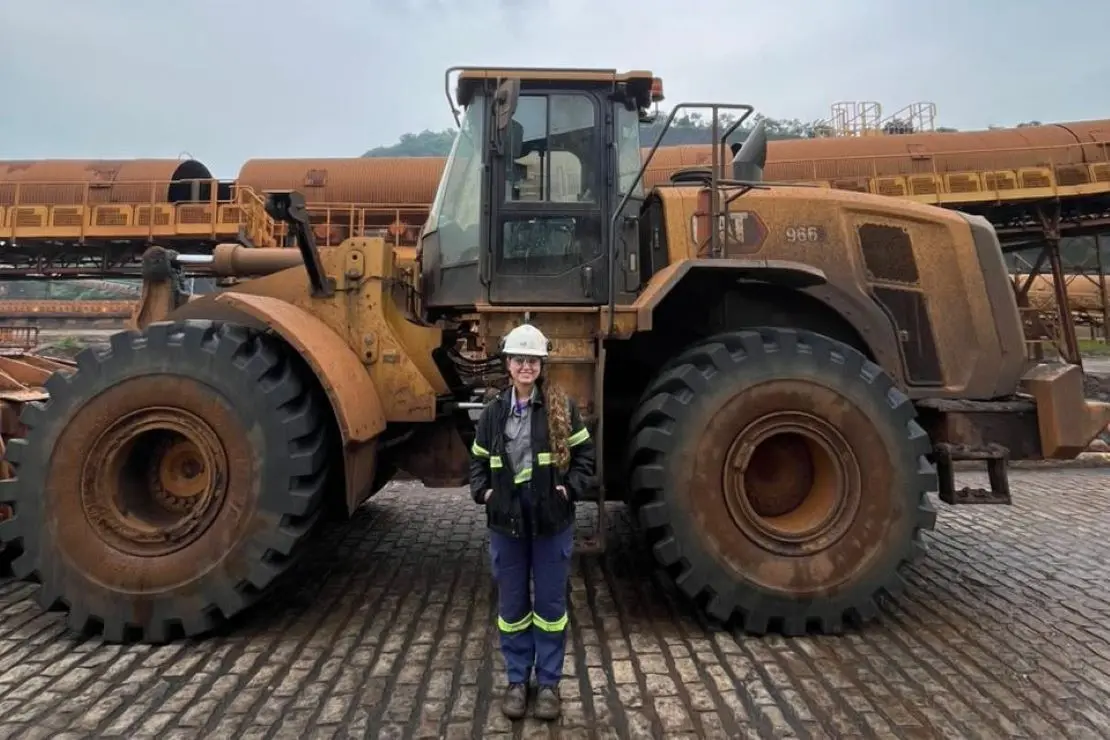 Colaboradora posando para foto em frente a uma máquina móvel pesada