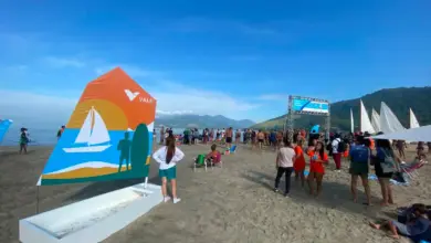Estrutura do 3º Festival Náutico montada na Praia do Saco, em Mangaratiba, com participantes circulando pela areia, embarcações à vela ao fundo e painel da Vale em destaque durante evento esportivo realizado à beira-mar