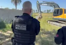 Agente da Polícia Militar observa uma retroescavadeira derrubando uma construção irregular