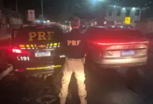Agente da Polícia Rodoviária Federal com viatura da PRF e veículo recuperado