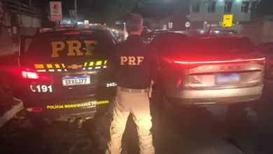 Agente da Polícia Rodoviária Federal com viatura da PRF e veículo recuperado