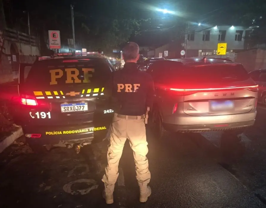 Agente da Polícia Rodoviária Federal com viatura da PRF e veículo recuperado