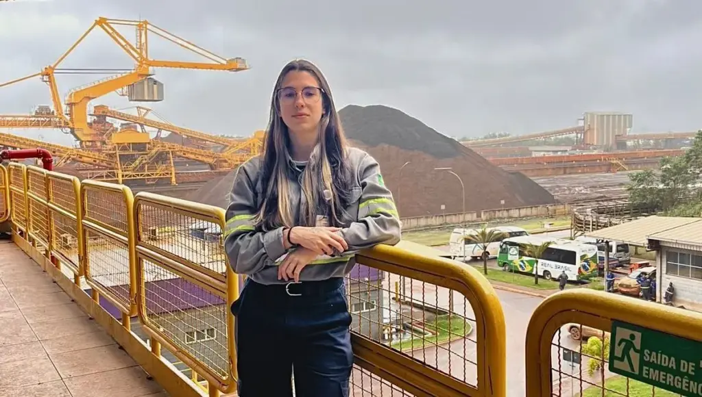Colaboradora do Porto Sudeste posando tendo ao fundo a planta industrial da empresa