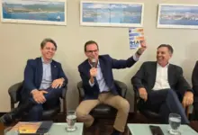 Facerj apresenta demanda ao Eduardo Paes, pré-candidato ao Governo do Estado do Rio de Janeiro, que aparece sentado ao centro da foto, falando ao microfone enquanto apresenta o livro “Economia do Mar”. Ao seu lado, representantes do setor empresarial acompanham o debate. O ambiente é decorado com fotografias de paisagens costeiras e portuárias, reforçando a temática do evento