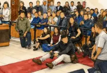 Ilustração baseada em fotografia da Sessão Solene pelos 208 anos de emancipação político-administrativa de Itaguaí mostra jornalistas, fotógrafos, cinegrafistas e produtores de conteúdo acomodados no chão e em cadeiras improvisadas para realizar a cobertura do evento no plenário da Câmara Municipal. A imagem foi editada com inteligência artificial para descaracterizar os rostos de todas as pessoas retratadas, preservando suas identidades sem alterar o contexto da cena.