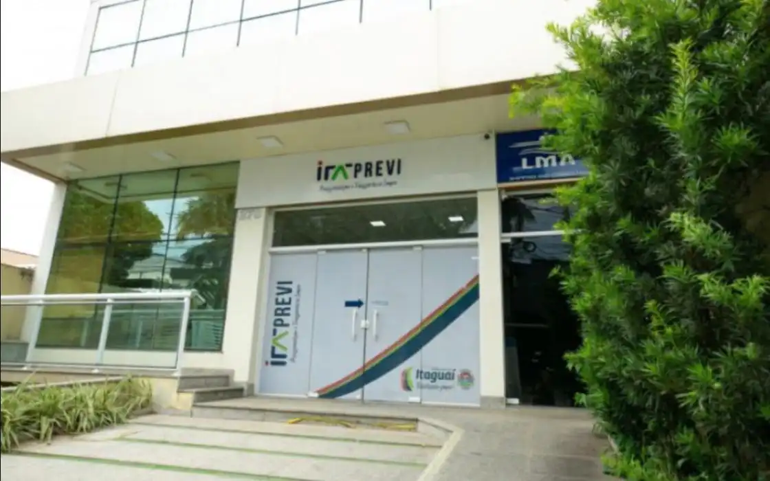 **Texto alternativo (alt):** Fachada do Instituto de Previdência Municipal de Itaguaí (ITAPREVI), com entrada principal em portas de vidro adesivadas com a identidade visual do instituto e da Prefeitura de Itaguaí. O prédio possui fachada envidraçada, rampa de acessibilidade à esquerda e árvores ao lado direito da entrada.