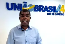 Donite de Jesus, vestindo camisa social azul, está na sede do partido em frente ao letreiro em que descreve União Brasil 44 no primeiro plano e Rio de Janeiro no segundo plano.