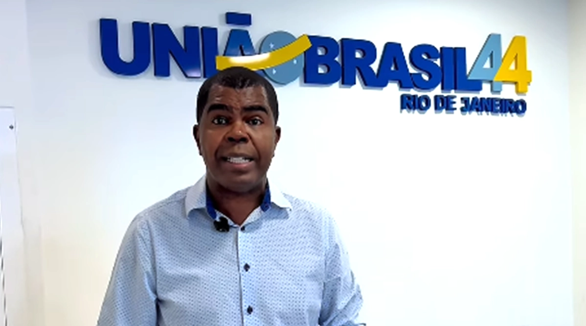 Donite de Jesus, vestindo camisa social azul, está na sede do partido em frente ao letreiro em que descreve União Brasil 44 no primeiro plano e Rio de Janeiro no segundo plano.