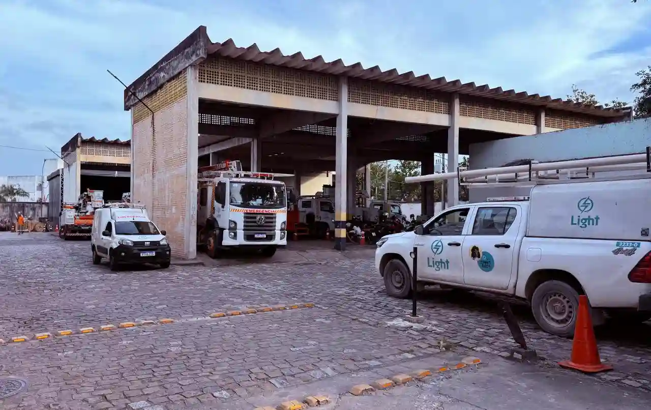 Vista do pátio da unidade da Light em Itaguaí, com diversas caminhonetes, caminhões e veículos operacionais estacionados sob um galpão. A imagem foi registrada durante apuração do Jornal Atual, enquanto bairros do município ainda enfrentavam falta de energia após o vendaval.