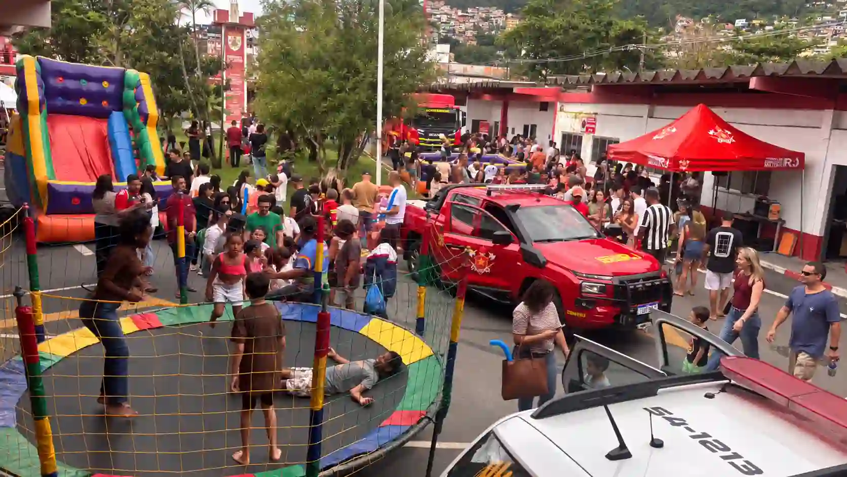 Crianças brincam em cama elástica e brinquedo inflável, enquanto famílias visitam o quartel do 10º GBM, com viaturas dos bombeiros em exposição.