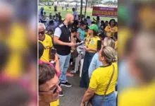Oficial de justiça com documento nas mãos conversa com Kelaine Goulart, de camisa amarela e boné verde, entre frequentadores da feira de Itaguaí.