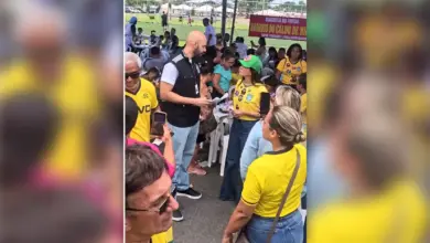 Oficial de justiça com documento nas mãos conversa com Kelaine Goulart, de camisa amarela e boné verde, entre frequentadores da feira de Itaguaí.
