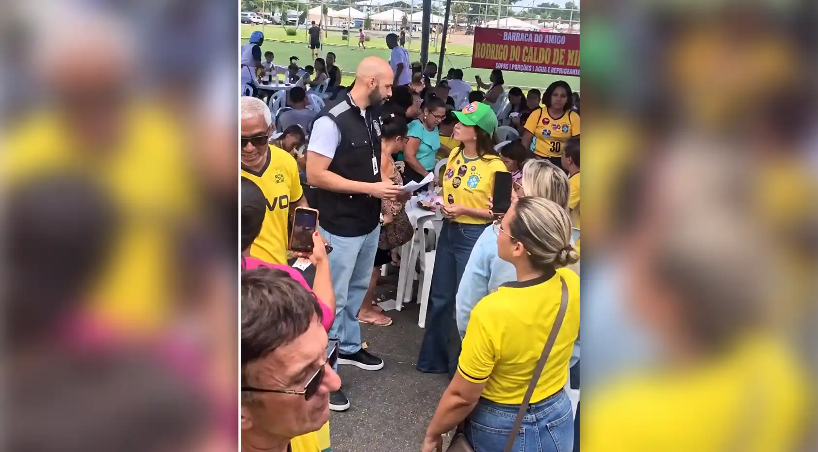 Oficial de justiça com documento nas mãos conversa com Kelaine Goulart, de camisa amarela e boné verde, entre frequentadores da feira de Itaguaí.
